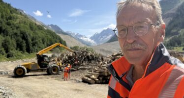 Auf dem Schuttkegel in Blatten bearbeitet eine Steinfräse die Testflächen für die Rekultivierung. Gleichzeitig fliegt ein Helikopter Bäume und Äste, die durch den Bergsturz zerstört worden sind, aus dem Wald. Kanal9 auf Reportage mit Manfred Bötsch, Mitglied Aufbaukommission Blatten 2030.