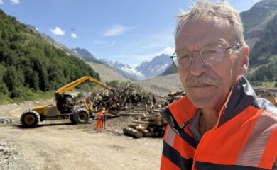 Auf dem Schuttkegel in Blatten bearbeitet eine Steinfräse die Testflächen für die Rekultivierung. Gleichzeitig fliegt ein Helikopter Bäume und Äste, die durch den Bergsturz zerstört worden sind, aus dem Wald. Kanal9 auf Reportage mit Manfred Bötsch, Mitglied Aufbaukommission Blatten 2030.